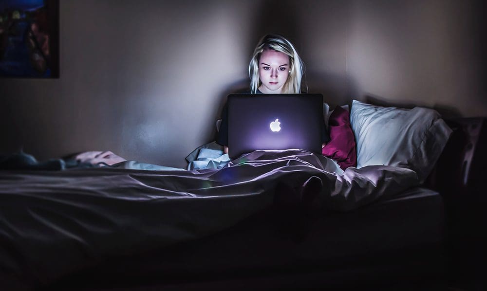 Girl sitting on a bed watching a video about a business.